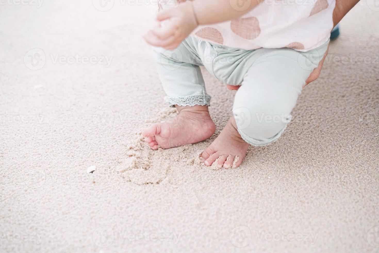 kleine voet van babymeisje op zandstrand. voor het eerst op zand lopen. foto