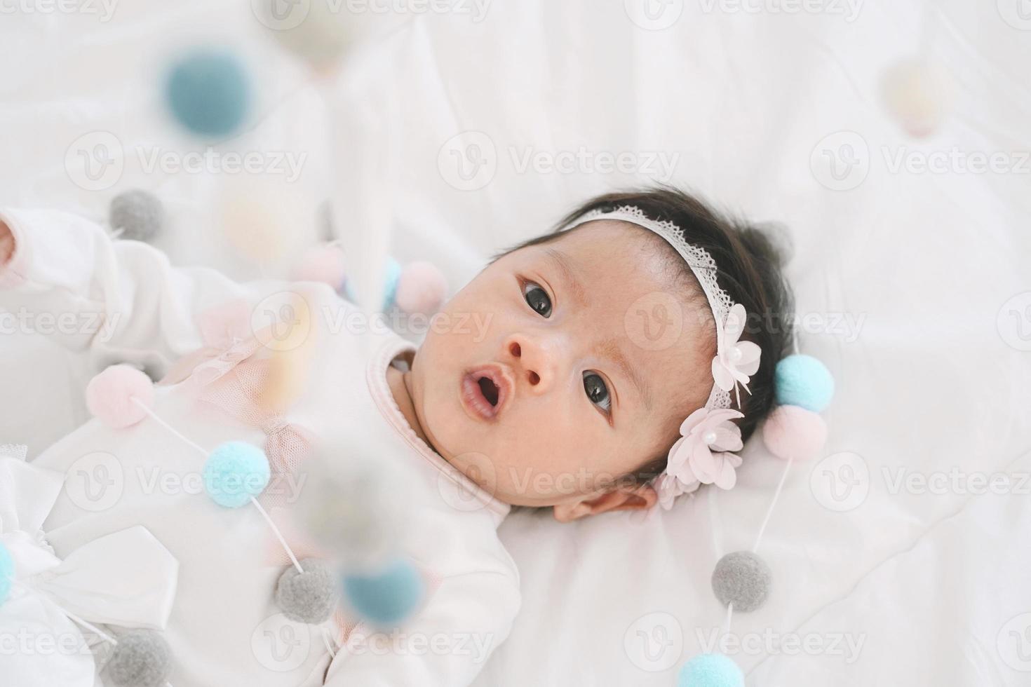 schattig klein babymeisje in een mooie jurk kijken naar babywieg mobiel thuis. babybed mobiel. speelgoed boven de wieg. hangende zachte ballen voor het kind. foto