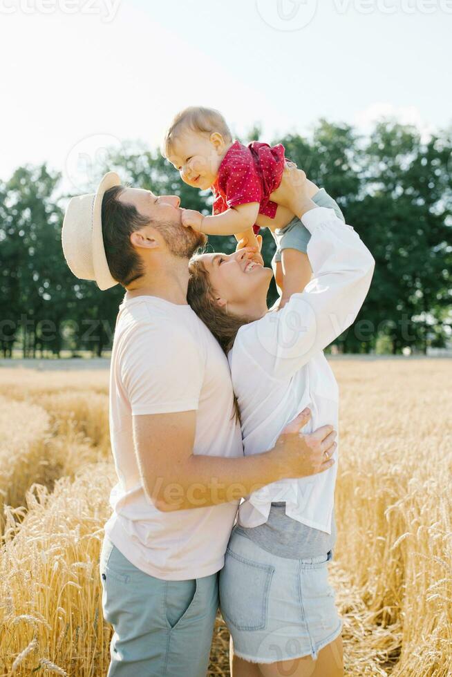 een jong moeder, vader en weinig zoon genieten natuur samen in de vers lucht. een gelukkig familie met een kind wandelingen door een tarwe veld- en geniet de zoet momenten van hun leven foto