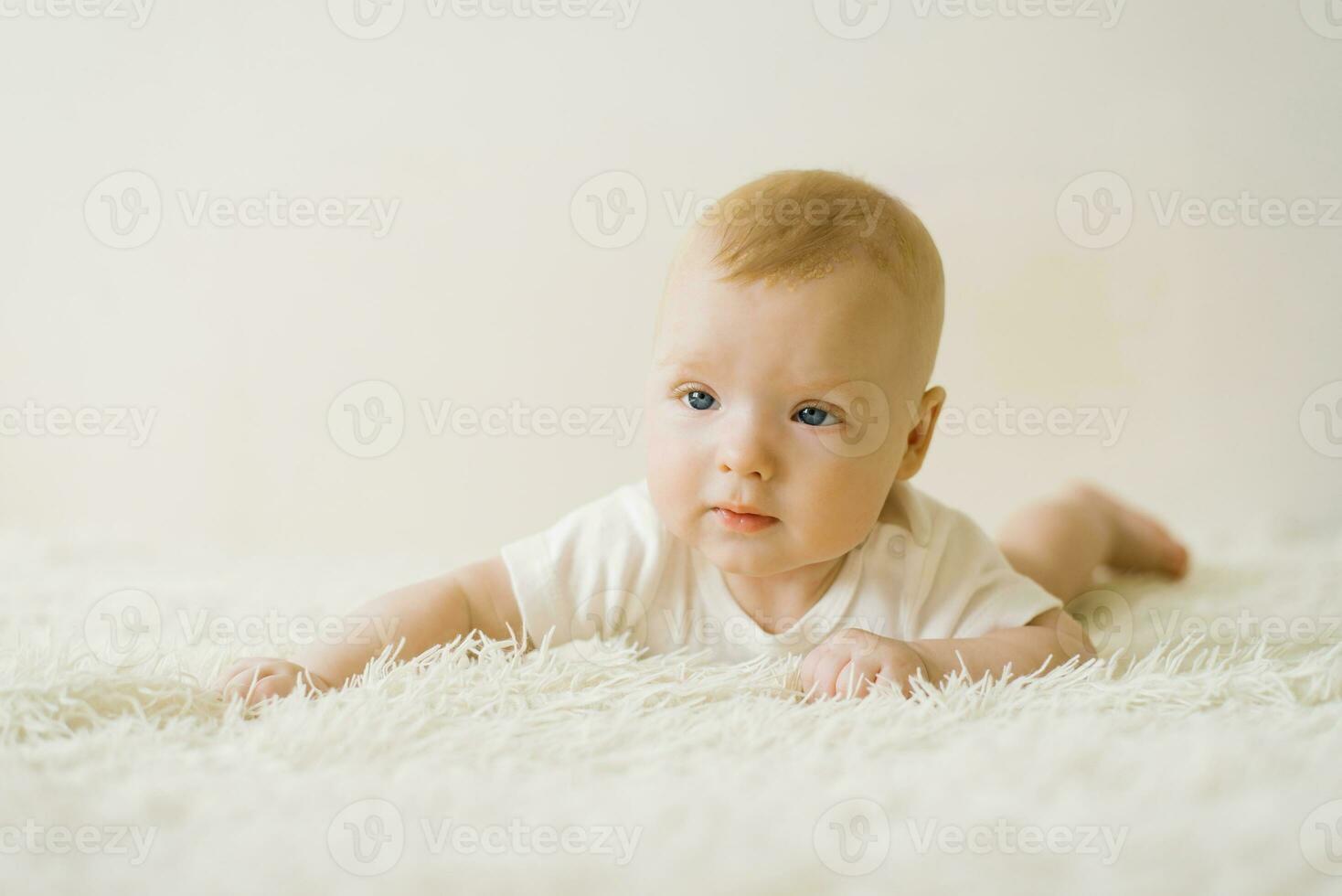 een vijf maanden oud baby is aan het liegen Aan zijn maag Aan de bed. de concept van zorgzaam voor een baby foto