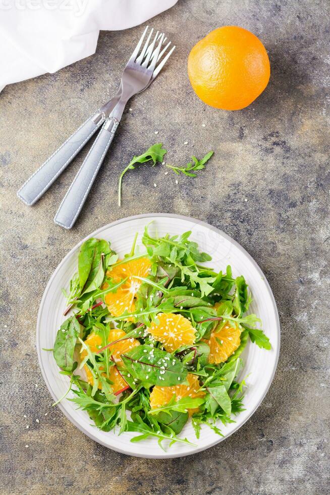 eetpatroon vegetarisch vitamine salade van oranje stukken en mengen van rucola, snijbiet en mizun bladeren Aan een bord Aan de tafel. top en verticaal visie foto