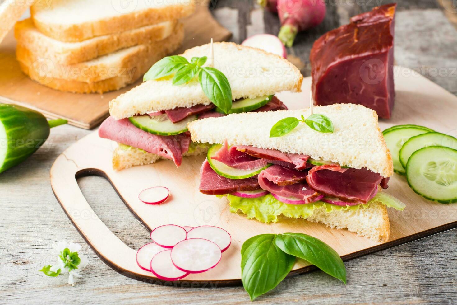 vers wit brood boterhammen met pastrami, komkommer, radijs en basilicum Aan een snijdend bord. Amerikaans tussendoortje. rustiek stijl foto