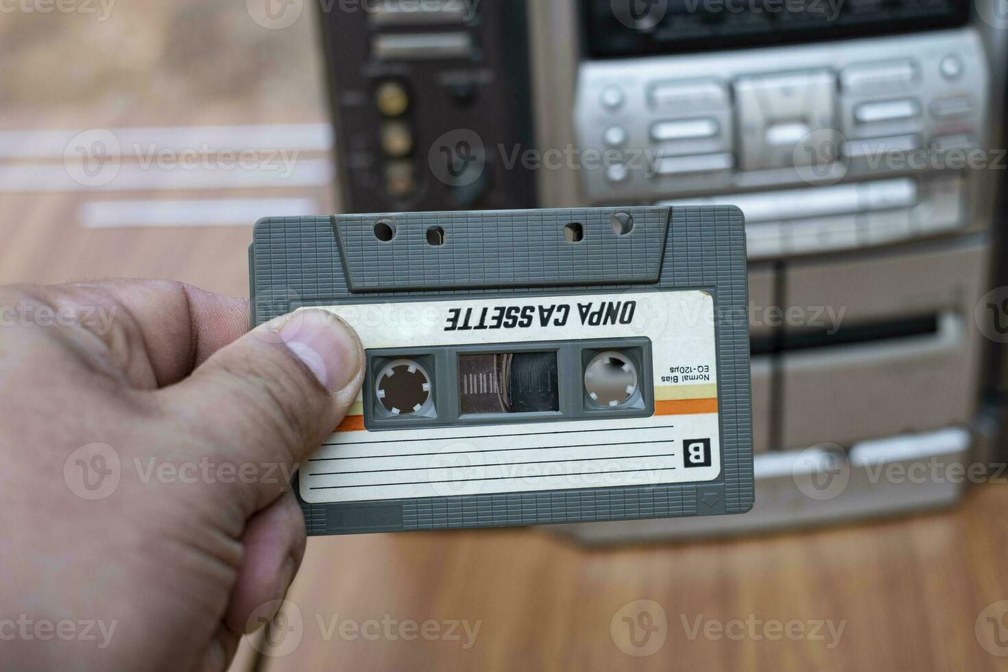 vrouwenhand die cassette in ouderwetse audiocassettespeler op hoogste bureau houten achtergrond zet foto