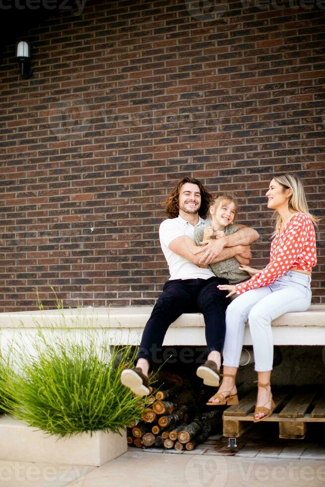 familie met een moeder, vader en dochter zittend buiten Aan de stappen van een voorkant veranda van een steen huis foto