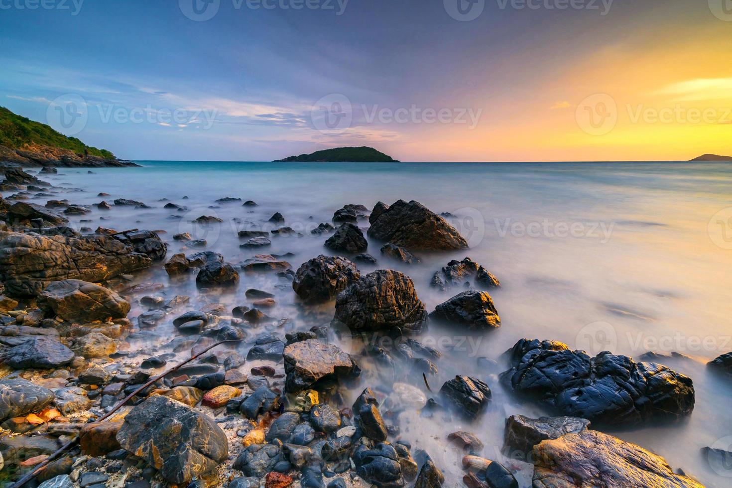 lange belichtingsopname van rotsen op de zee bij zonsondergang foto