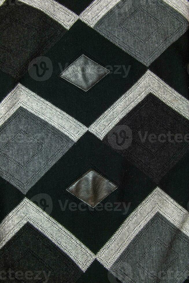 gedetailleerd inzetstukken in zwart oprecht leer Aan een gebreid wollen achtergrond met een abstract patroon. abstract kleding stof textuur. foto