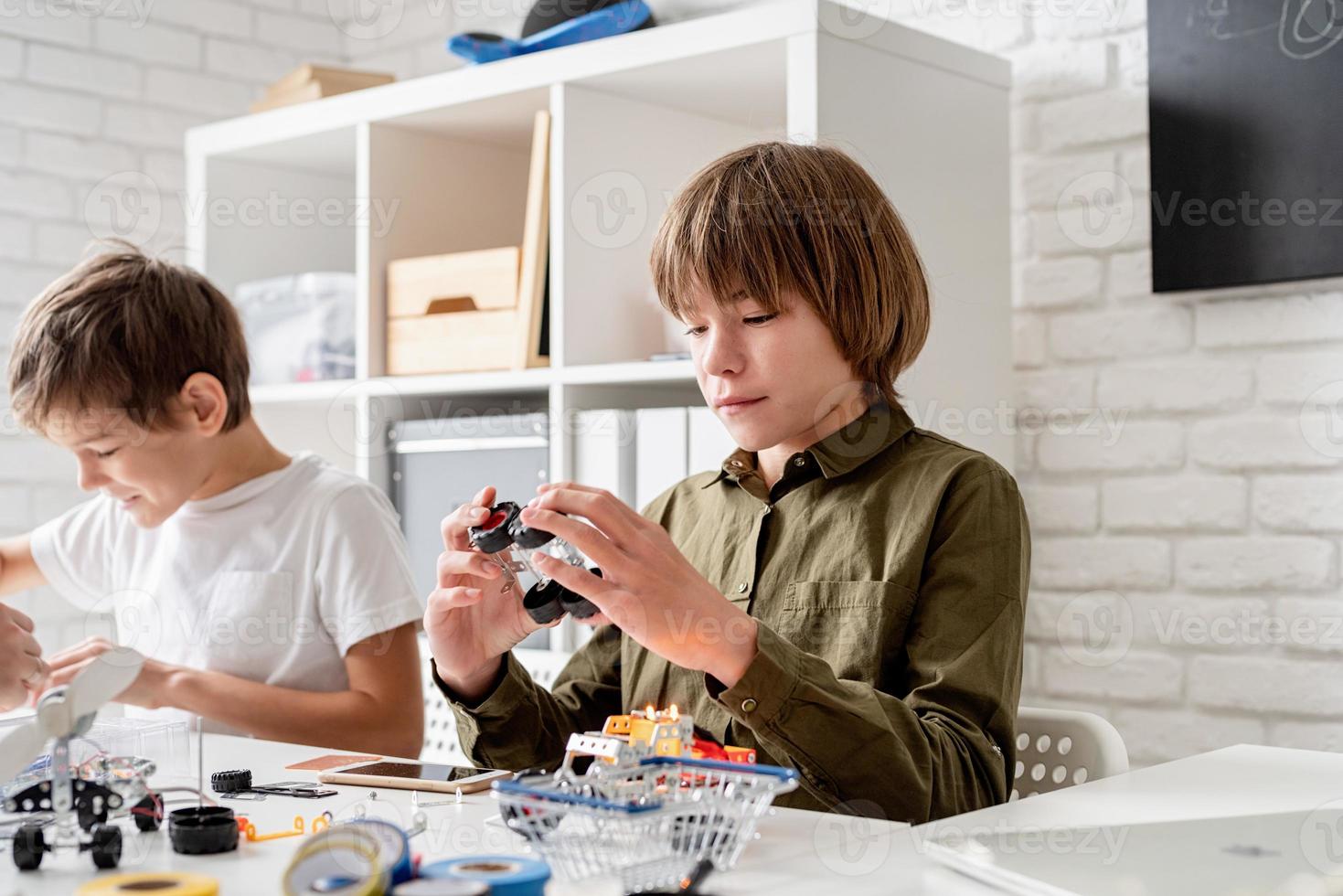 jonge jongens die plezier hebben met het bouwen van robotauto's in de werkplaats foto