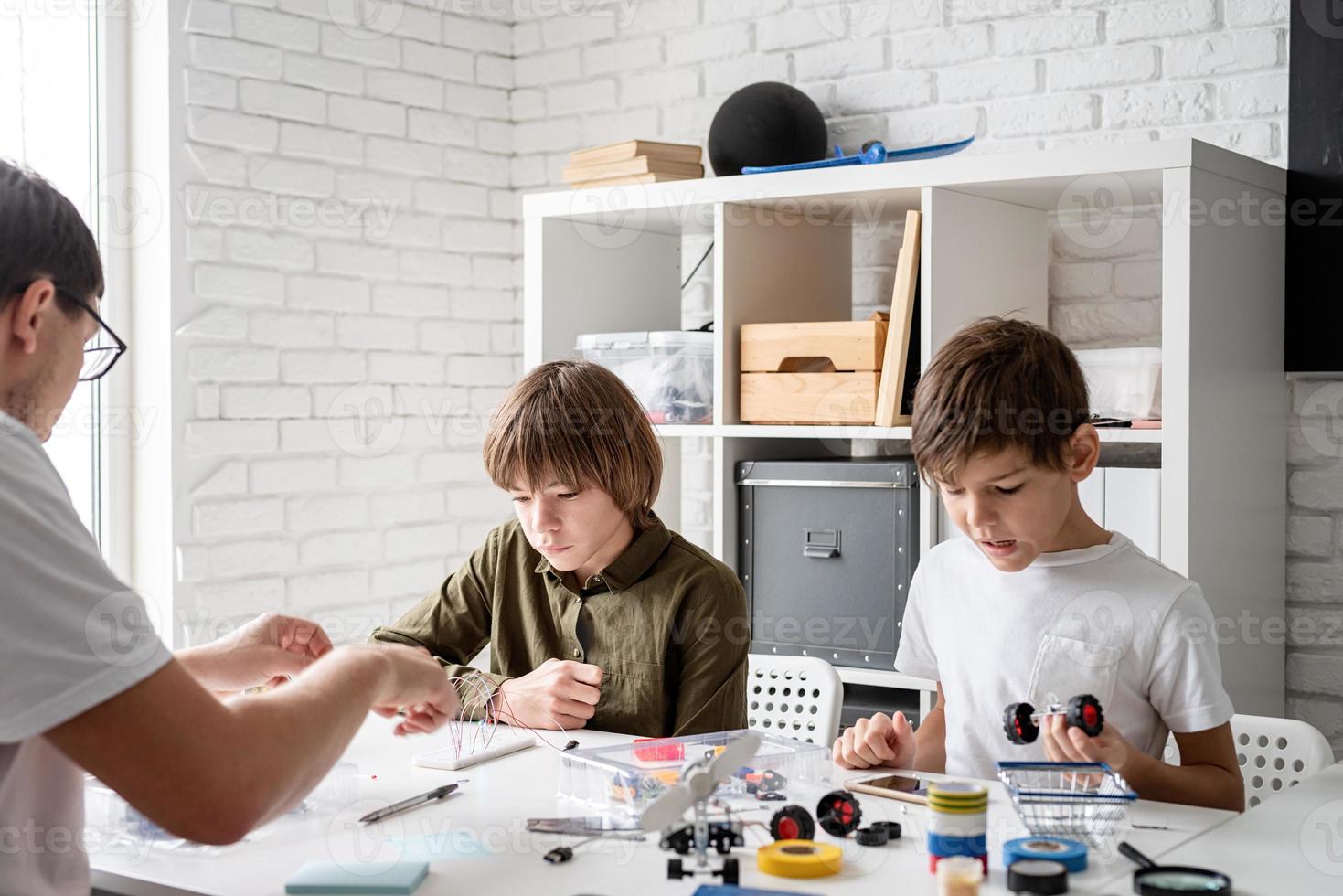 jonge jongens en leraar die plezier hebben met het bouwen van robotauto's in de werkplaats foto