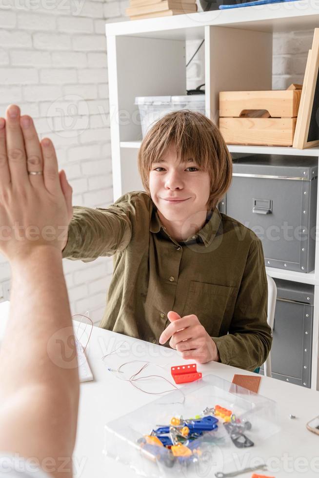 jonge jongens en leraar die plezier hebben met het bouwen van robotauto's in de werkplaats die high five doen foto