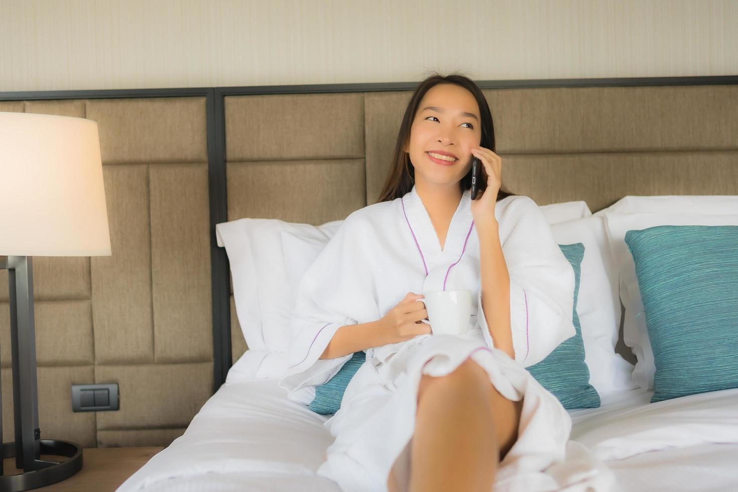 portret mooie jonge Aziatische vrouwen met behulp van mobiele smartphone met koffiekopje op bed foto