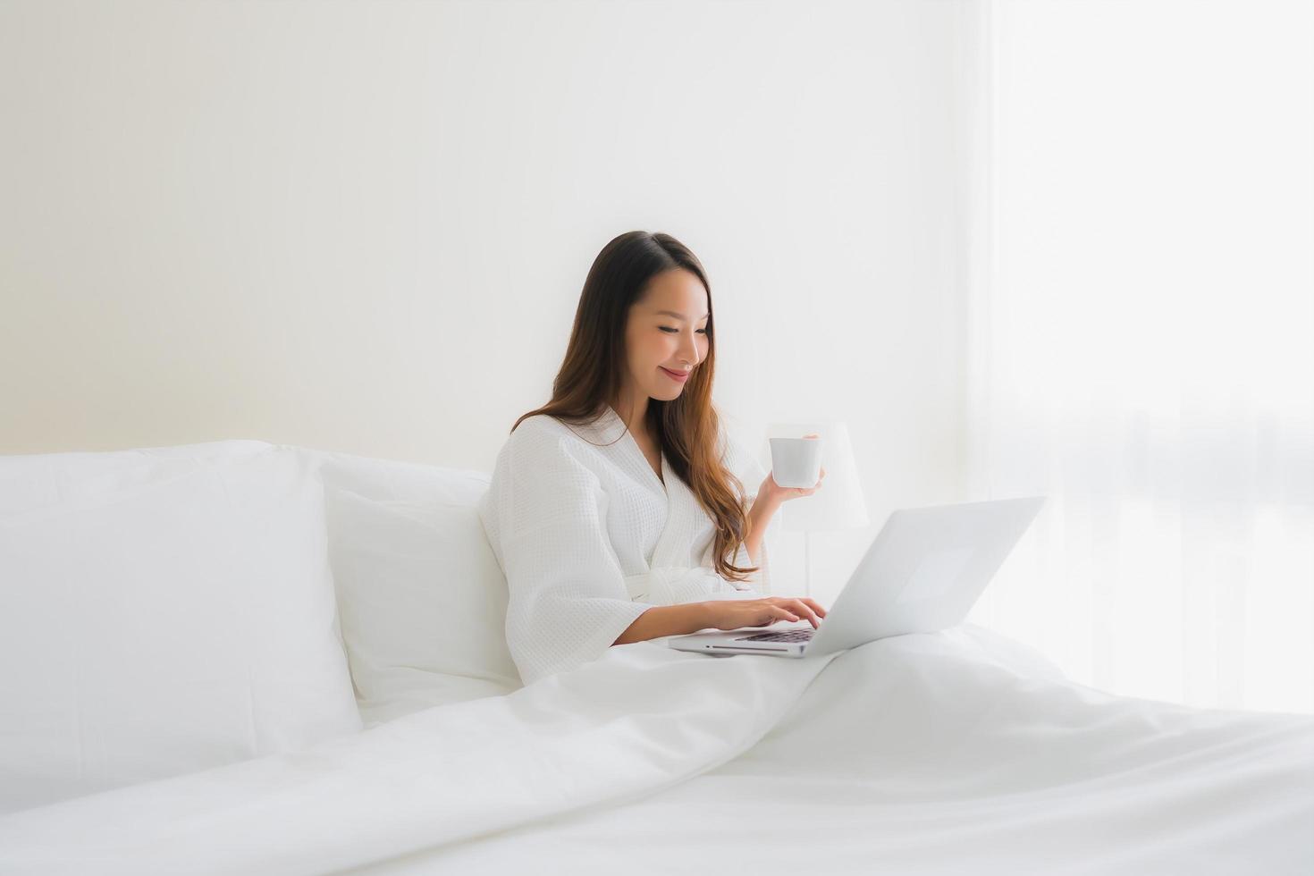 portret mooie jonge Aziatische vrouwen met koffiekopje en computer laptop op bed foto