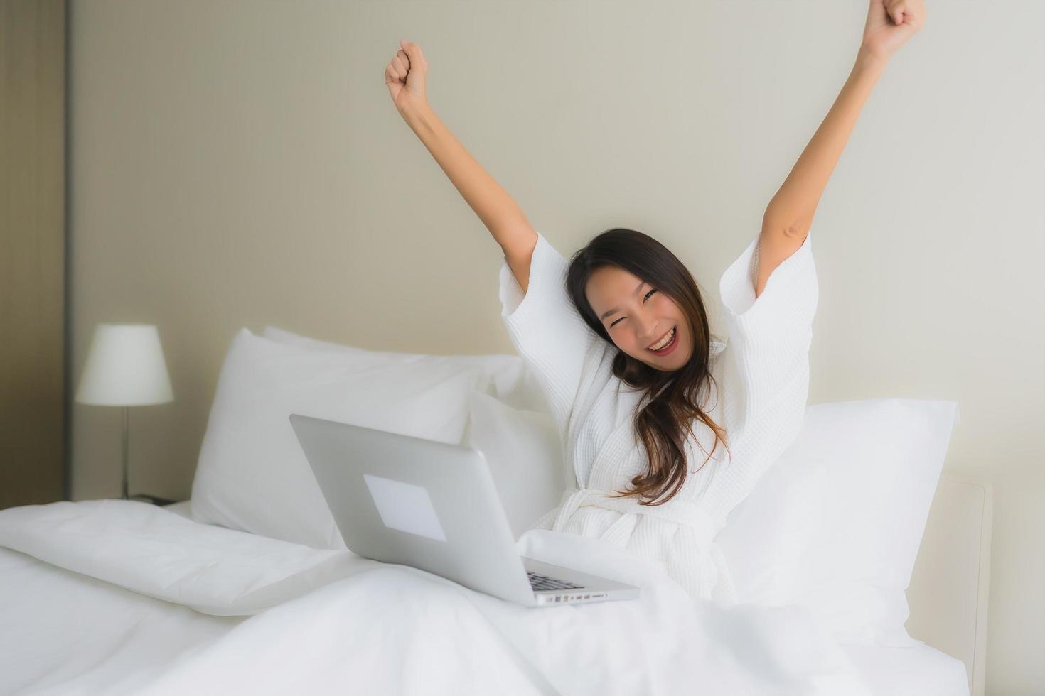 portret mooie jonge Aziatische vrouwen met koffiekopje en computer laptop op bed foto