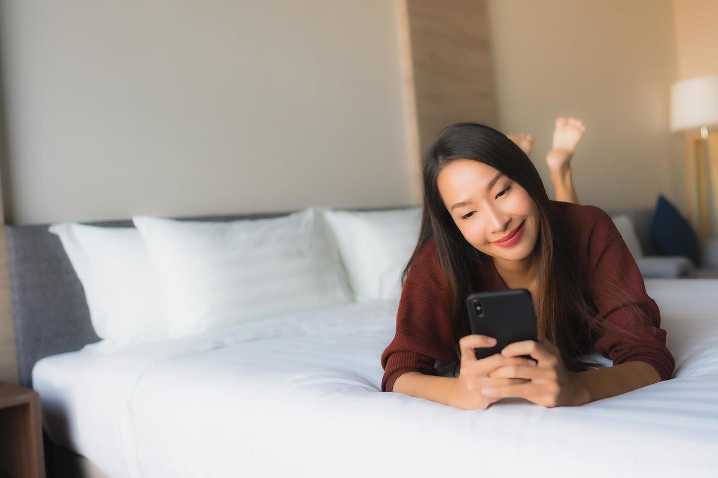 portret mooie jonge aziatische vrouwen die mobiele telefoon op bed gebruiken foto