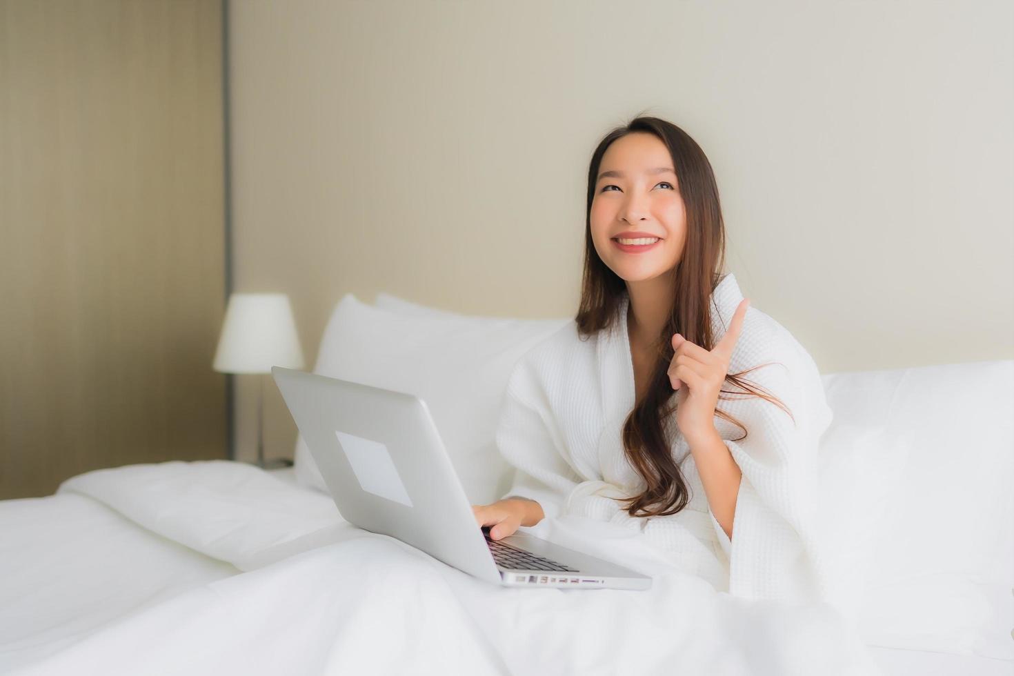 portret mooie jonge Aziatische vrouwen met koffiekopje en computer laptop op bed foto