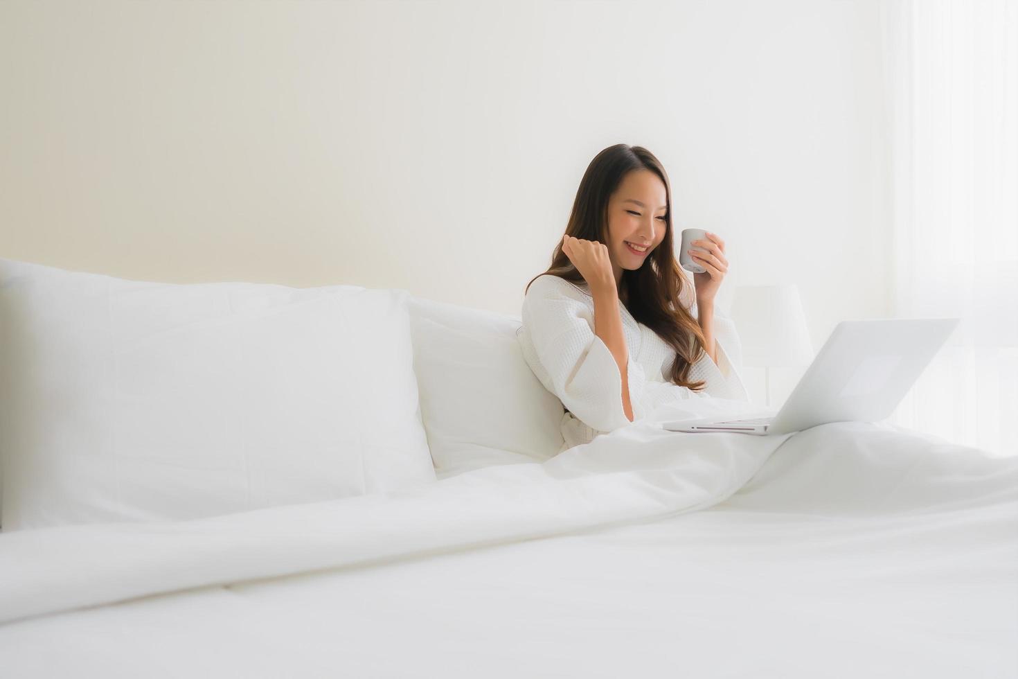 portret mooie jonge Aziatische vrouwen met koffiekopje en computer laptop op bed foto