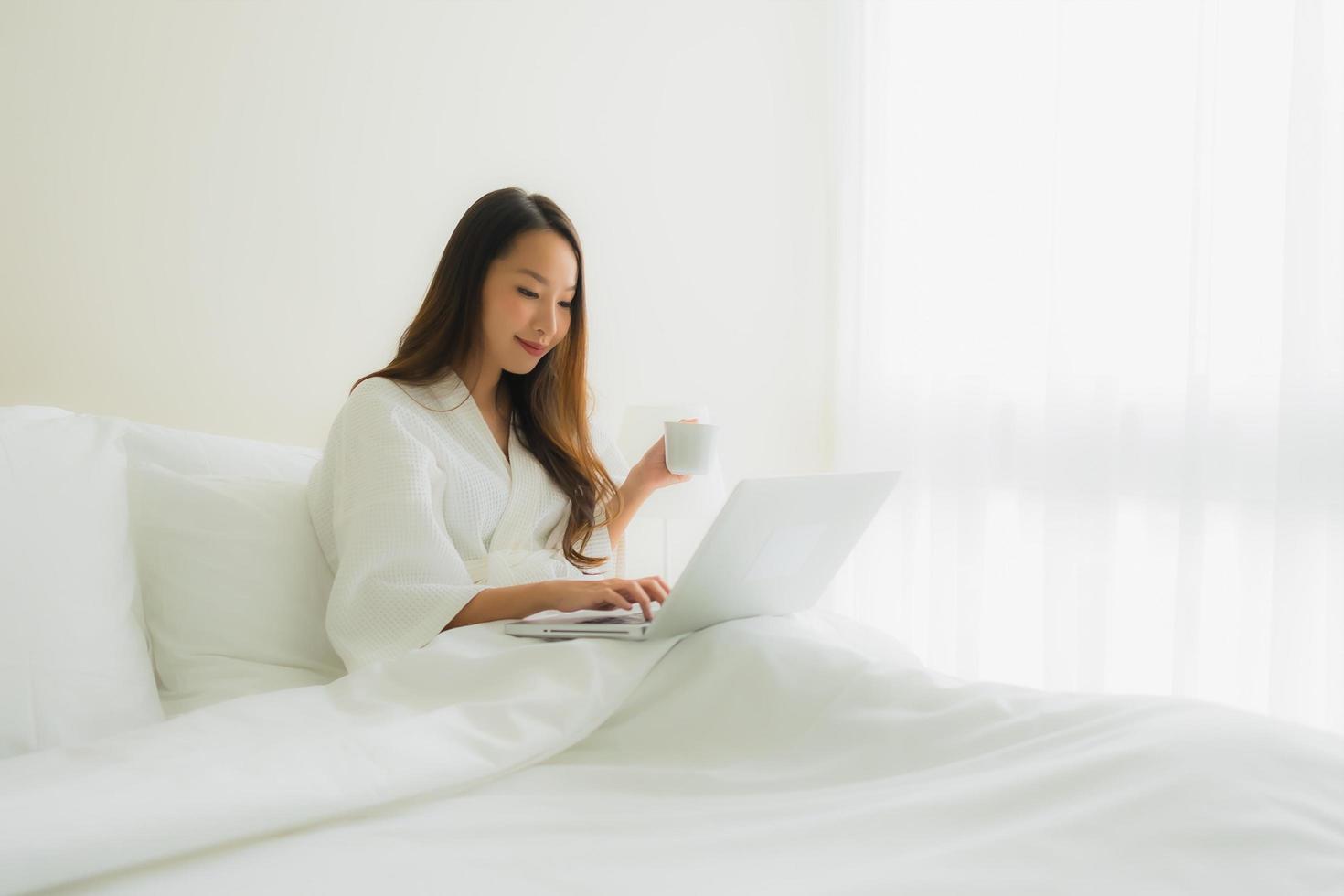 portret mooie jonge Aziatische vrouwen met koffiekopje en computer laptop op bed foto