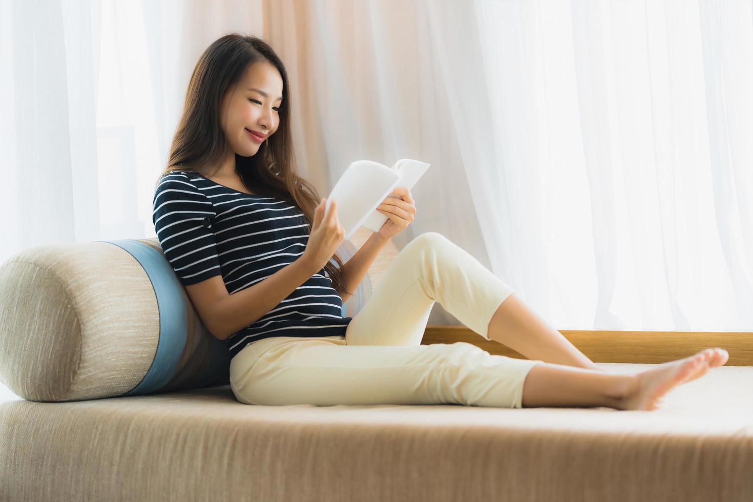 portret mooie jonge aziatische vrouw die een boek leest op de bank in de woonkamer foto