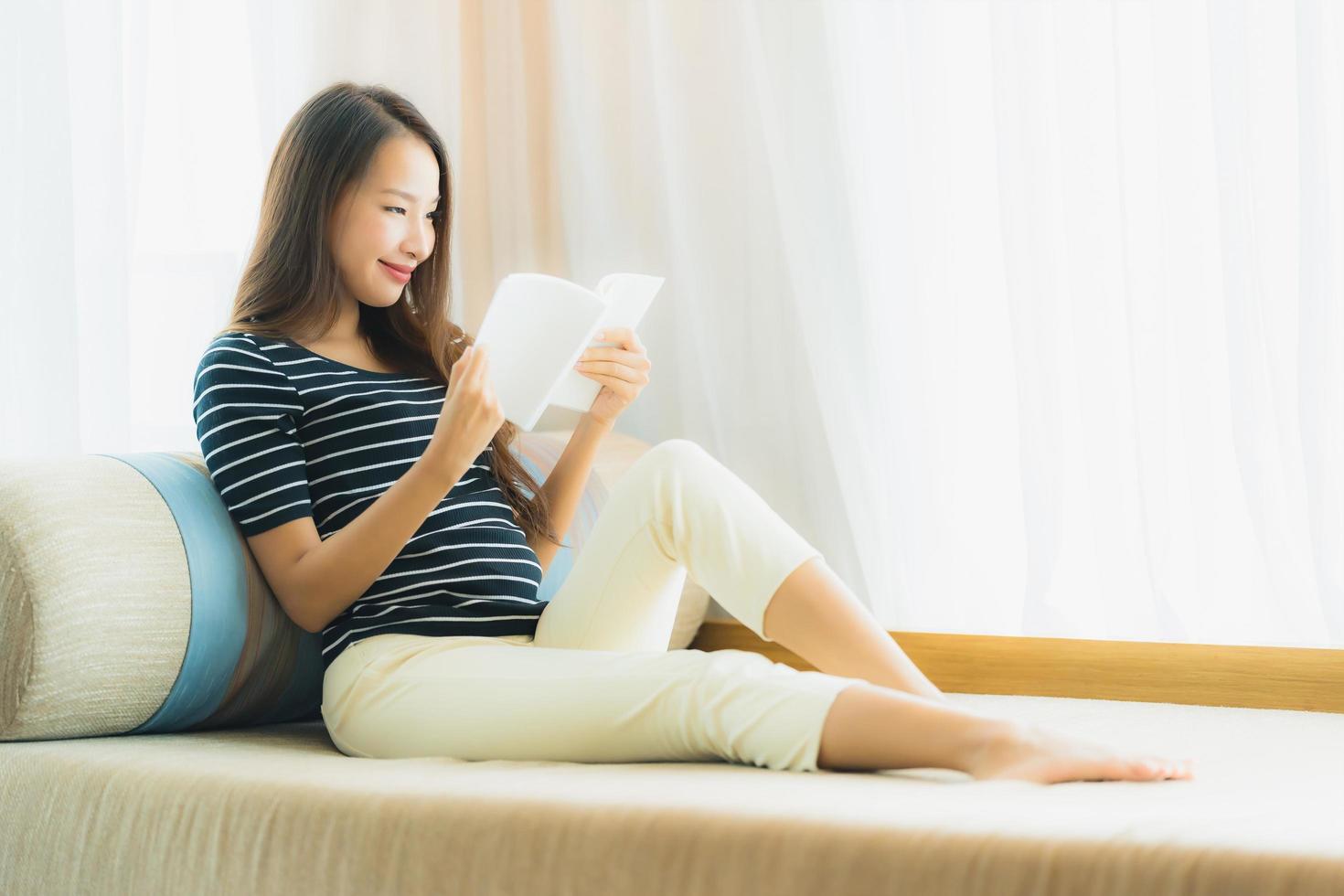 portret mooie jonge aziatische vrouw die een boek leest op de bank in de woonkamer foto