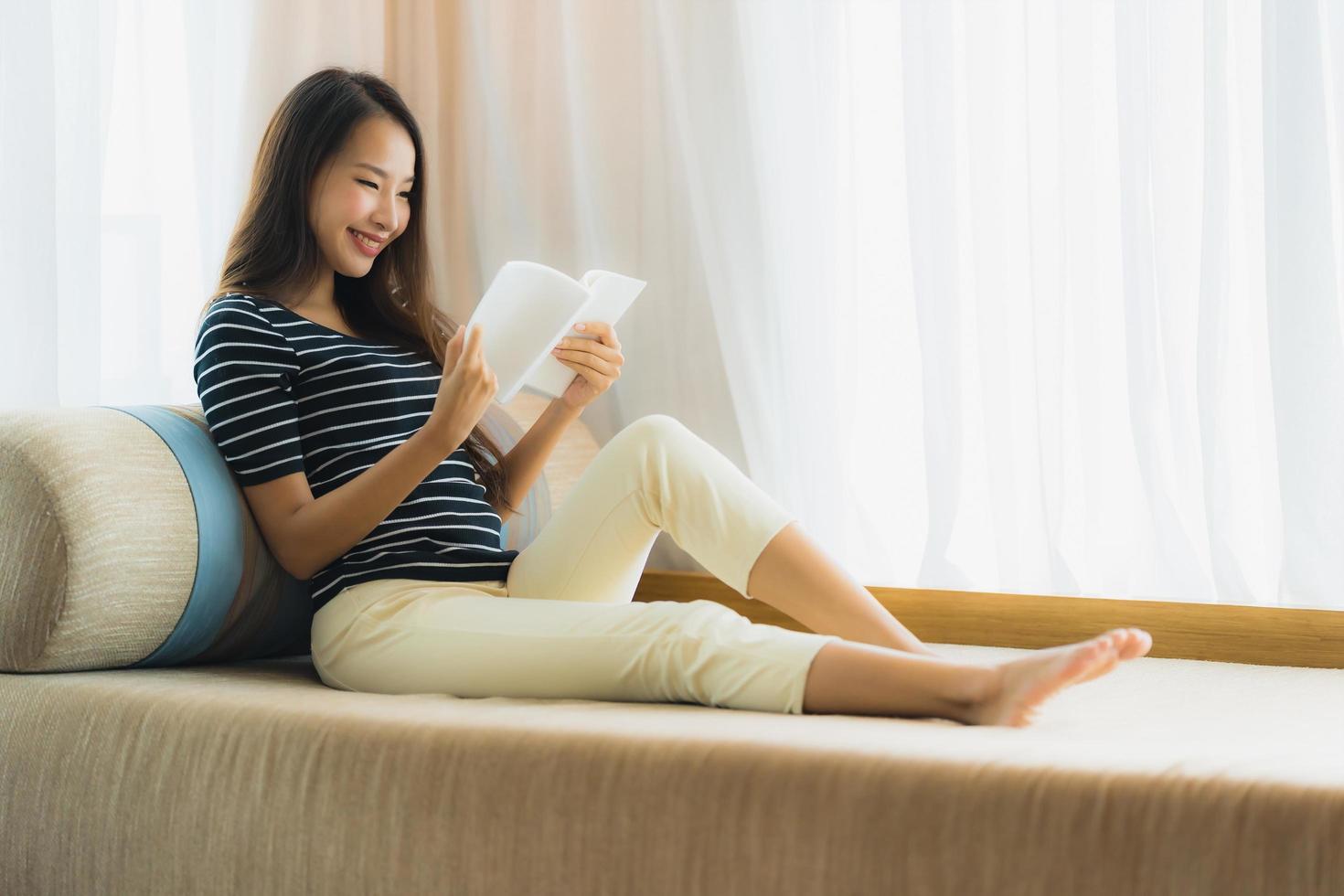 portret mooie jonge aziatische vrouw die een boek leest op de bank in de woonkamer foto