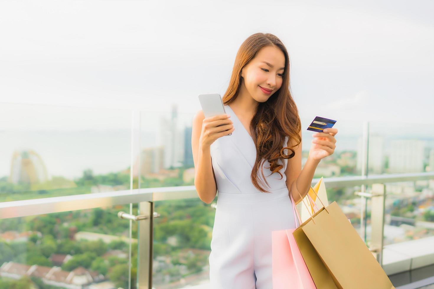 portret mooie jonge aziatische vrouw blij en glimlach met creditcard en mobiel of smartphone en boodschappentas foto