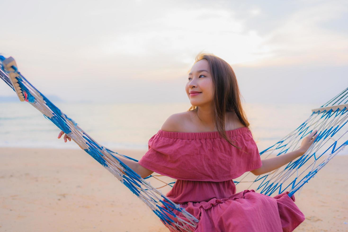 portret mooie jonge aziatische vrouw zittend op de hangmat met glimlach gelukkig dichtbij strand zee en oceaan foto