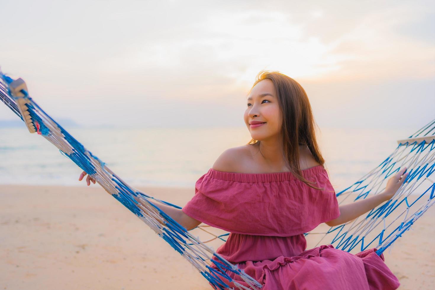portret mooie jonge aziatische vrouw zittend op de hangmat met glimlach gelukkig dichtbij strand zee en oceaan foto