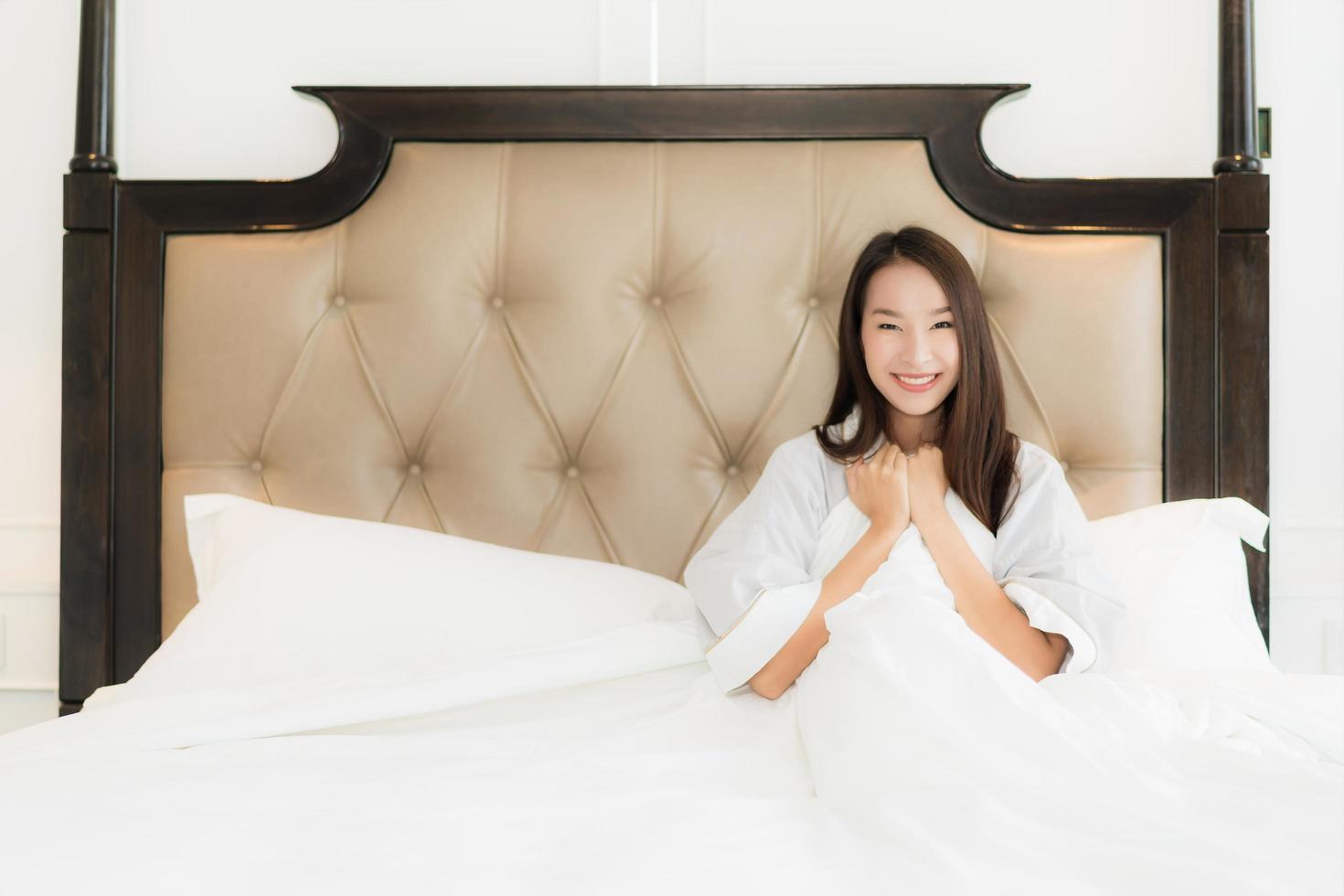 portret mooie jonge aziatische vrouw wakker met blij en glimlach op bed in slaapkamer interieur foto