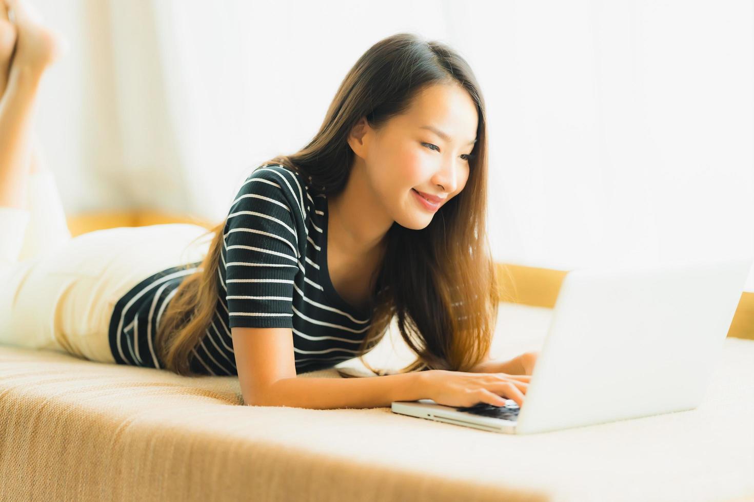 portret mooie jonge aziatische vrouw die computernotitieboekje of laptop op bank in woonkamer gebruikt foto