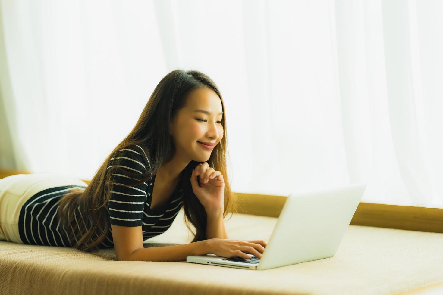 portret mooie jonge aziatische vrouw die computernotitieboekje of laptop op bank in woonkamer gebruikt foto