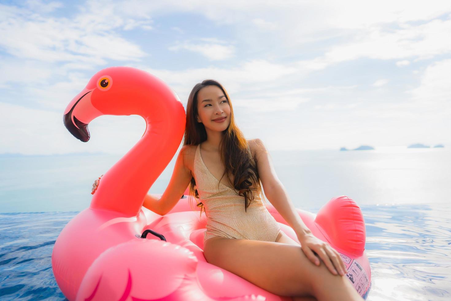 portret jonge aziatische vrouw op opblaasbare vlotterflamingo rond openluchtzwembad in hoteltoevlucht foto