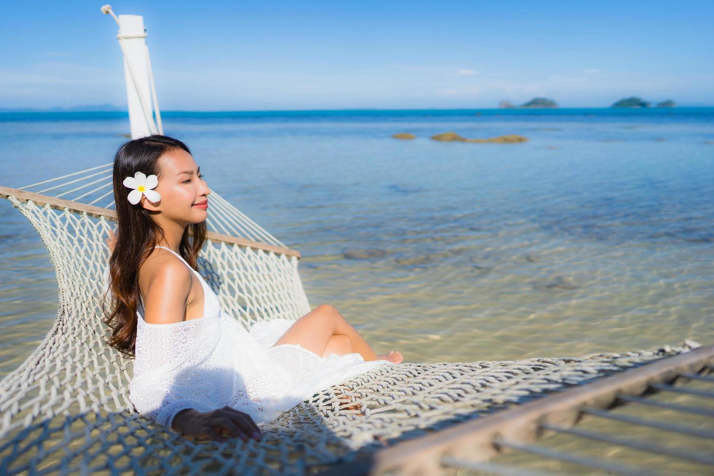 portret mooie jonge aziatische vrouw zittend op een hangmat rond zee strand oceaan om te ontspannen foto