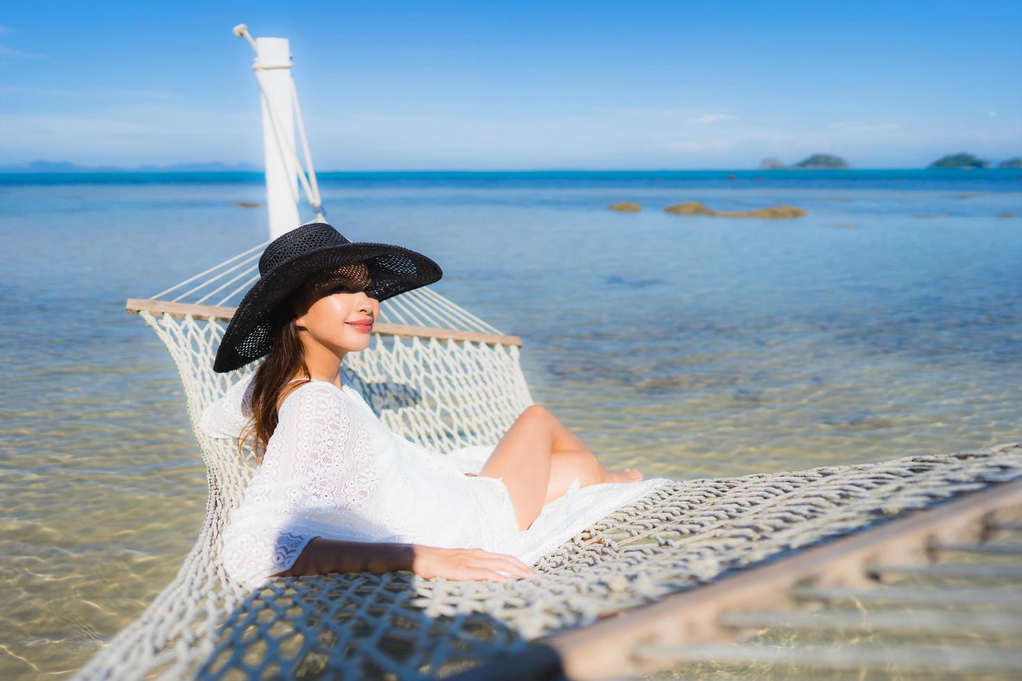 portret mooie jonge aziatische vrouw zittend op een hangmat rond zee strand oceaan om te ontspannen foto