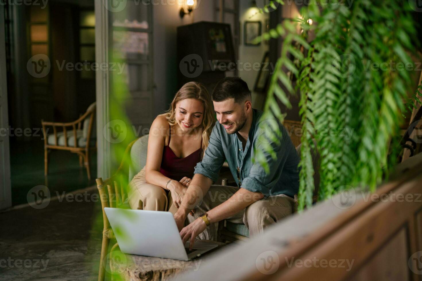 glimlachen etnisch man en vrouw browsen, surfen, aan het doen online boodschappen doen of aan het kijken film Aan pc apparaat, knuffelen zittend leven kamer tafel. concept van paren aan het doen vrij tijd activiteiten samen. foto