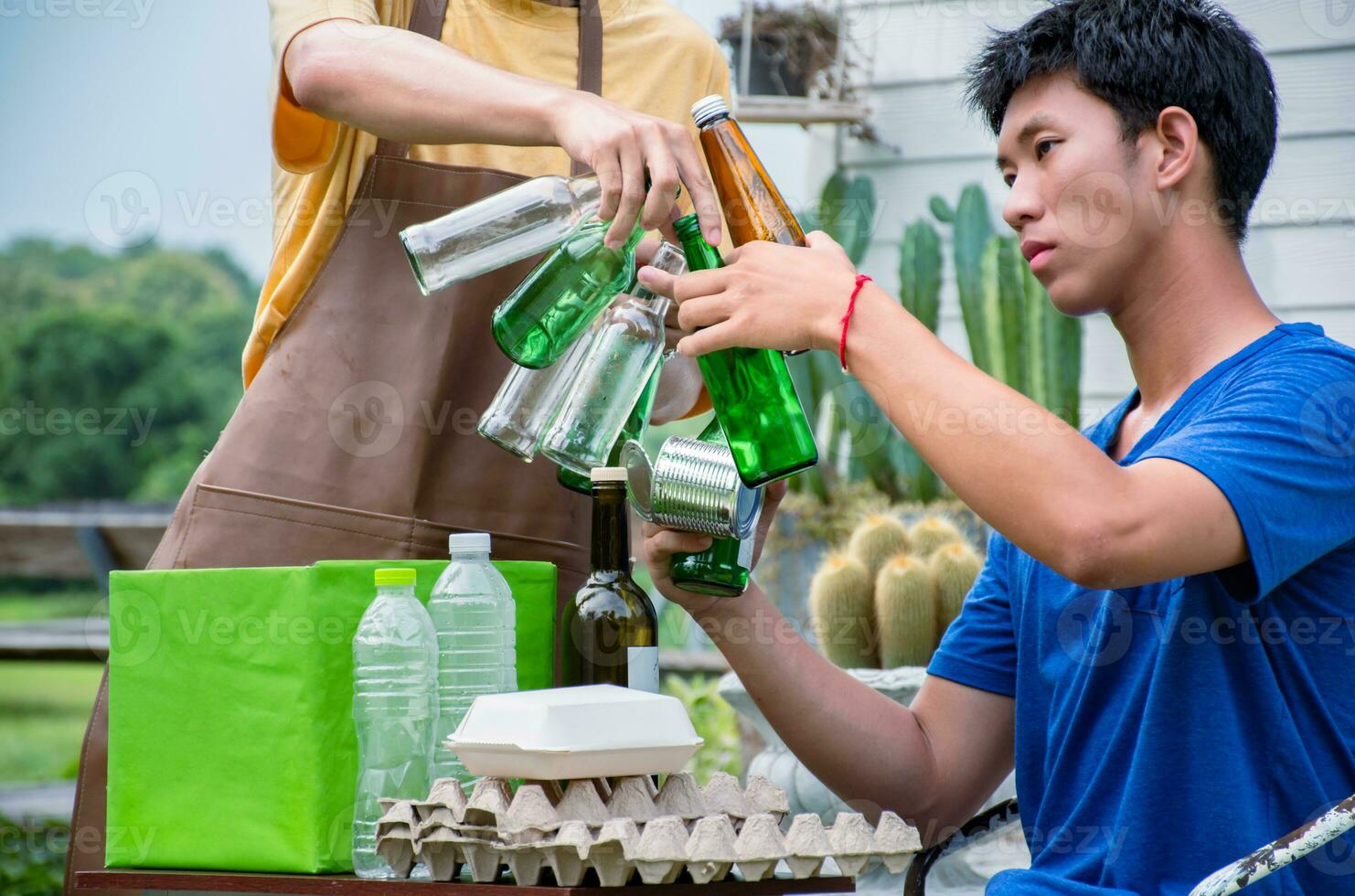 jong knap Aziatisch homo paren zijn scheiden huishoudens, flessen, blikjes, afval, papier, ei dienblad, in voorkant van hun huis, milieu zorg en globaal opwarming concept. foto