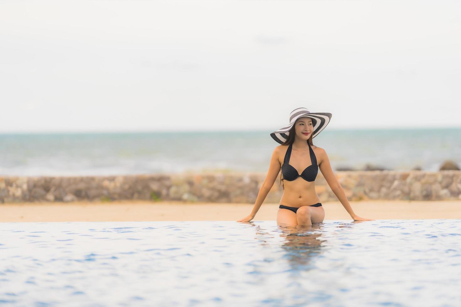 portret mooie jonge aziatische vrouw draagt bikini rond zwembad in hotelresort bijna zee oceaan strand foto