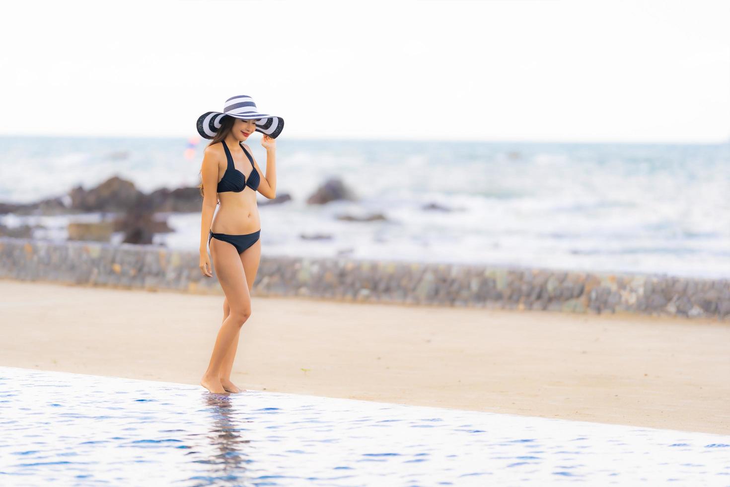 portret mooie jonge aziatische vrouw draagt bikini rond zwembad in hotelresort bijna zee oceaan strand foto