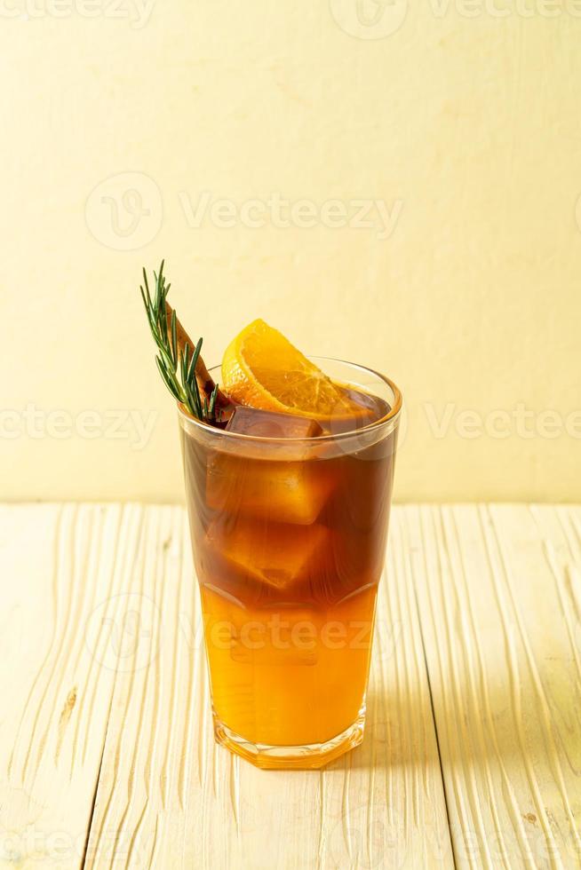 een glas iced americano zwarte koffie en een laagje sinaasappel- en citroensap versierd met rozemarijn en kaneel op een houten ondergrond foto