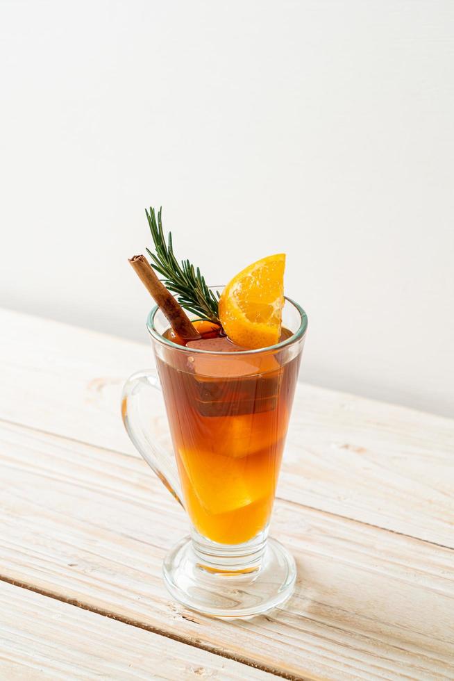 een glas iced americano zwarte koffie en een laagje sinaasappel- en citroensap versierd met rozemarijn en kaneel op een houten ondergrond foto