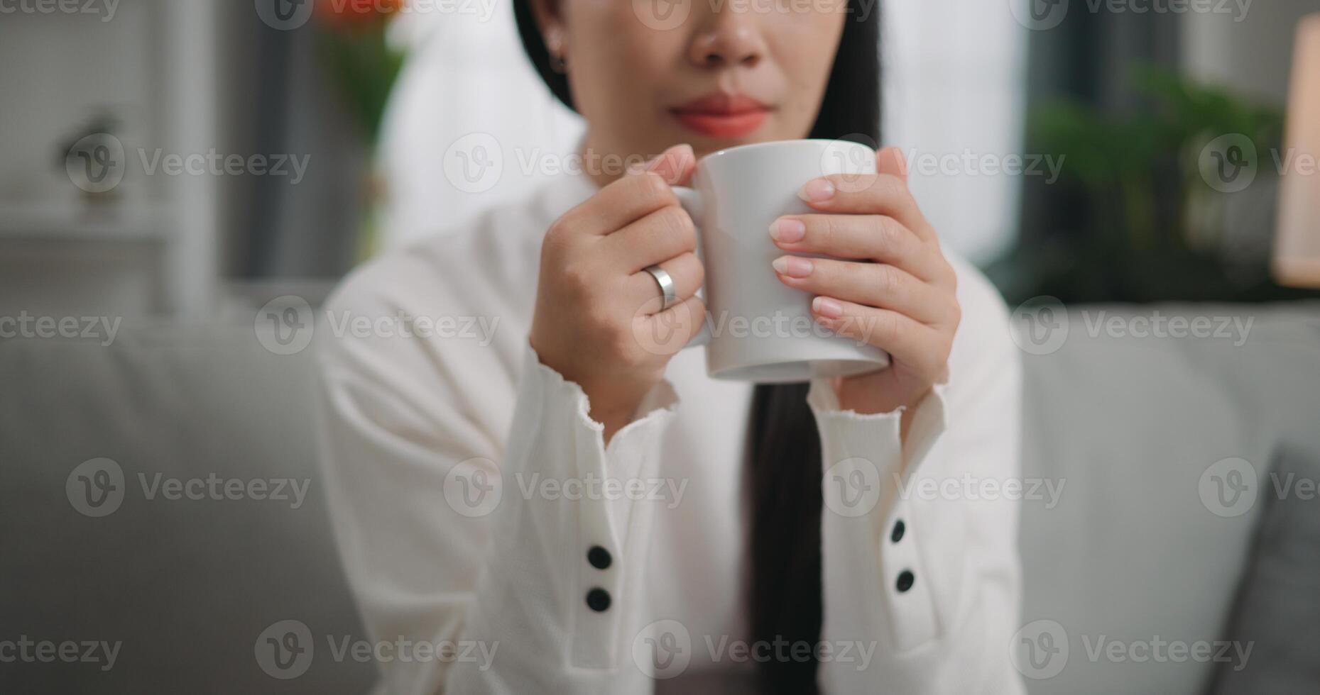 Aziatisch vrouw drinken een koffie terwijl zittend Aan de sofa foto