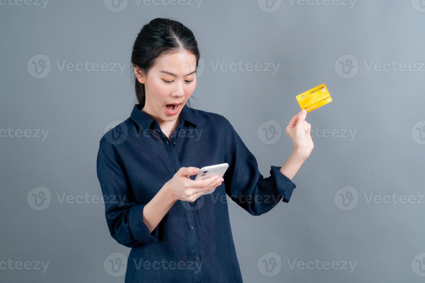 jong Aziatisch meisje dat een plastic creditcard toont terwijl ze een mobiele telefoon vasthoudt foto