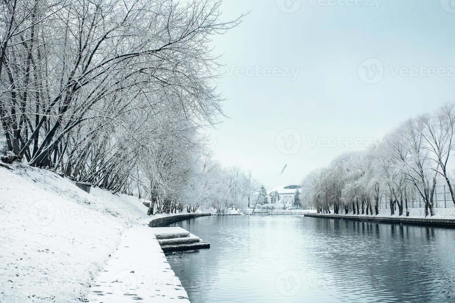 winter in de stad - sneeuw op de oevers van de rivier en op de bomen bedekt met vorst foto