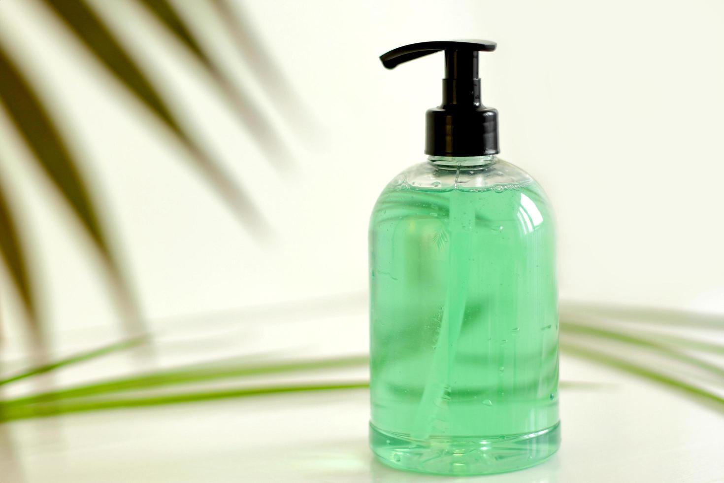 plastic fles met groene vloeibare zeep op een witte achtergrond met groene bladeren op de achtergrond foto