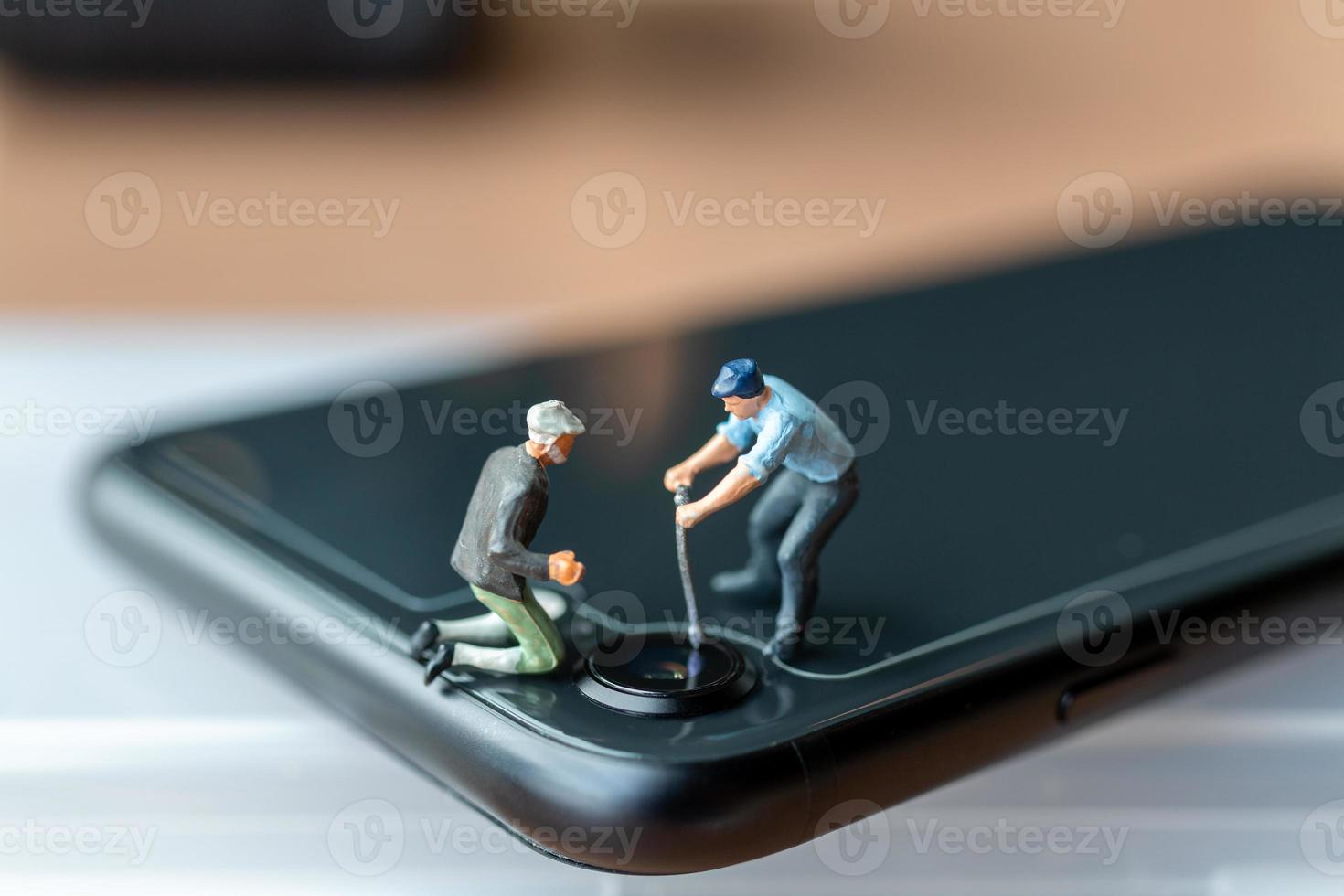 miniatuurmensenarbeider met hulpmiddelen die mobiele telefoon herstellen foto