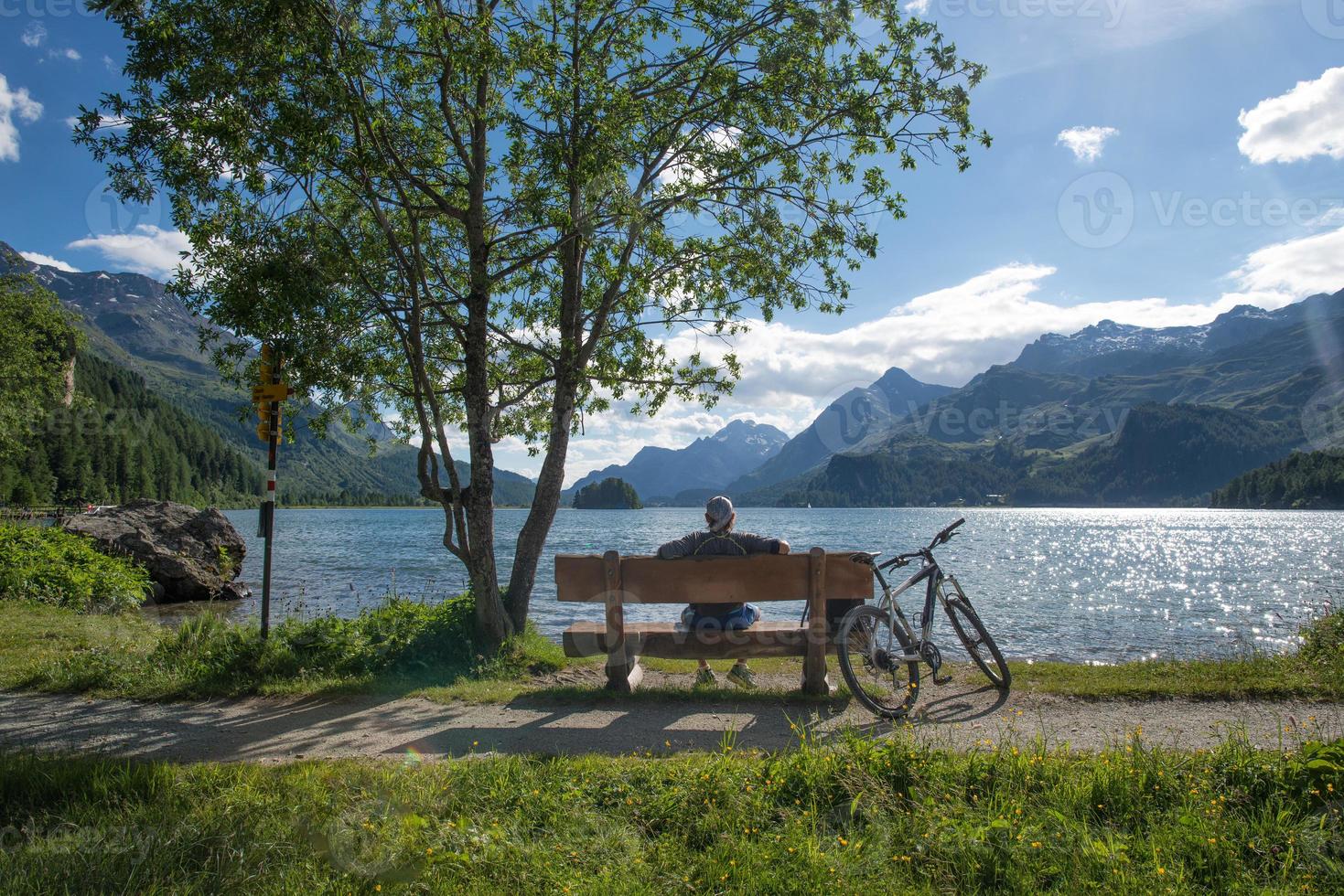 een fietser rust kijkend naar het uitzicht op een bankje voor een bergmeer foto