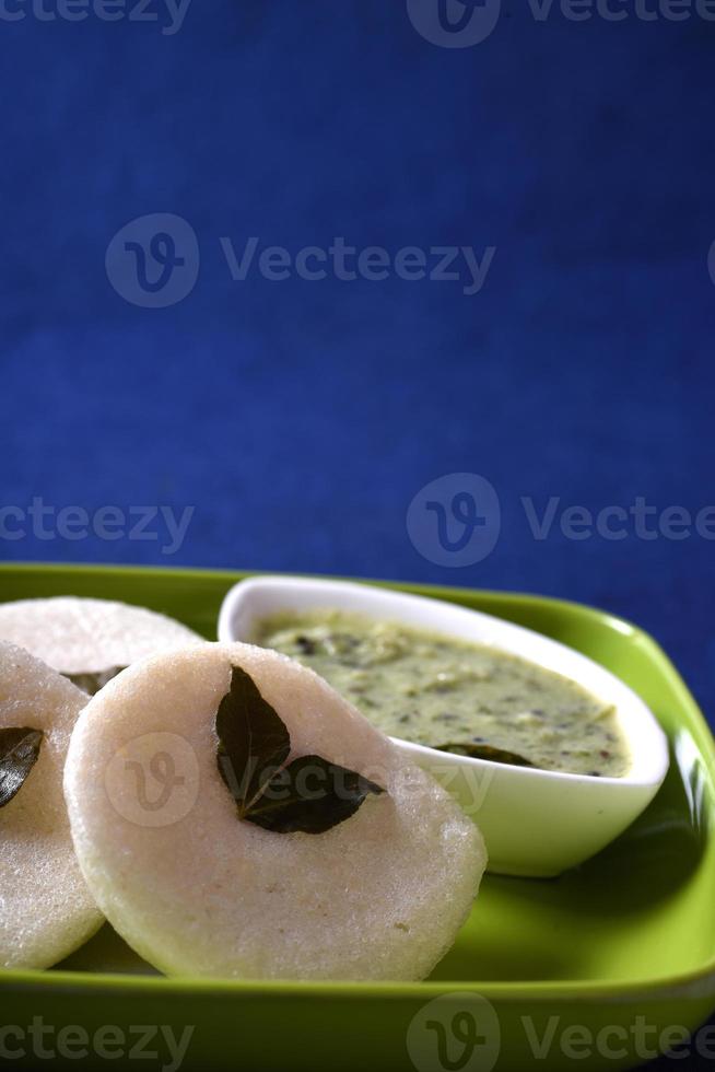 idli met kokos chutney op blauwe achtergrond, indiase schotel Zuid-indiase favoriete eten rava idli of griesmeel werkeloos of rava werkeloos, geserveerd met sambar en groene kokos chutney. foto