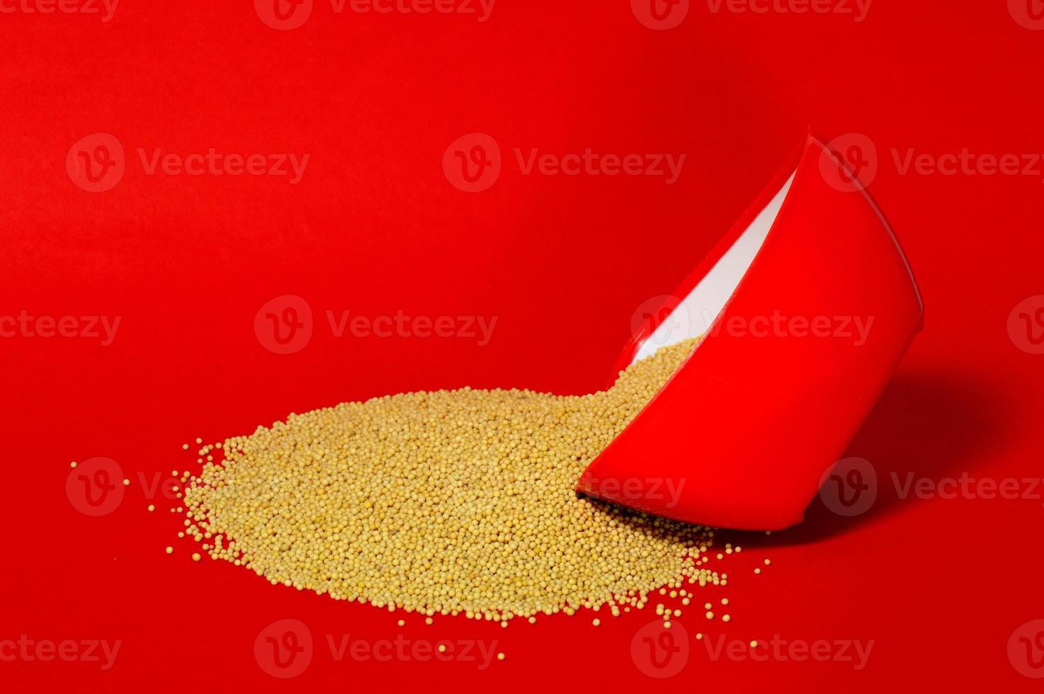 gele mosterdzaadjes in rode kom geïsoleerd op rode achtergrond foto