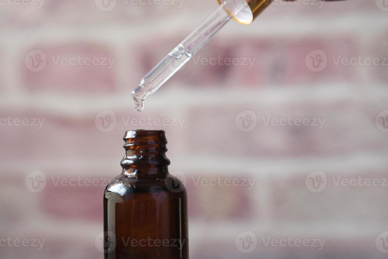 druppel valt van een pipet in een cosmetische fles foto