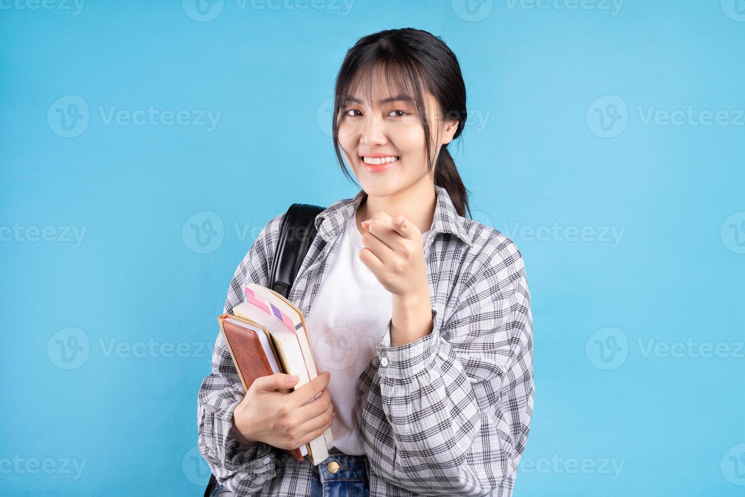 Aziatische vrouwelijke student met speelse uitdrukking op blauwe achtergrond foto