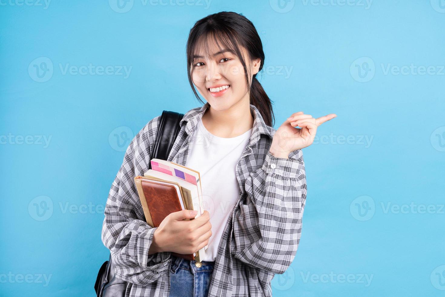 Aziatische vrouwelijke student met speelse uitdrukking op blauwe achtergrond foto