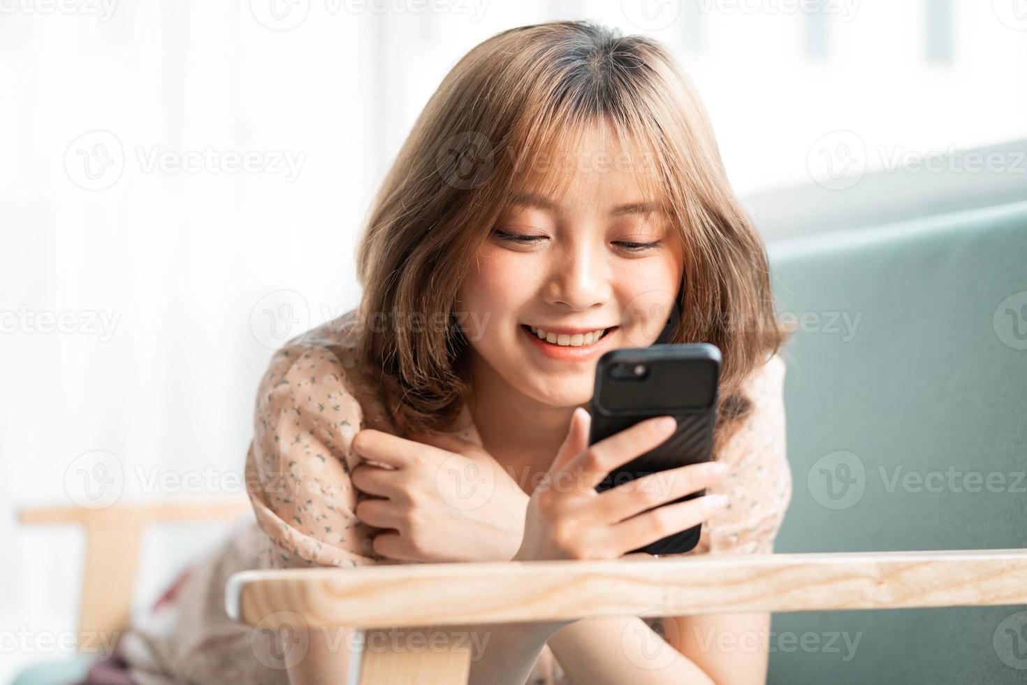 het jonge meisje lag languit op de bank met haar telefoon en glimlachte vrolijk foto